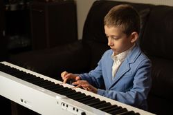 Young boy in blue blazer concentrating while playing piano.