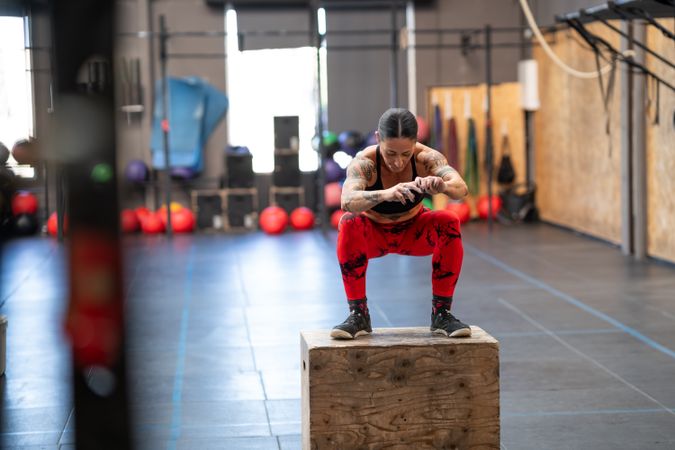 Woman squatting on a box in a gym after jump