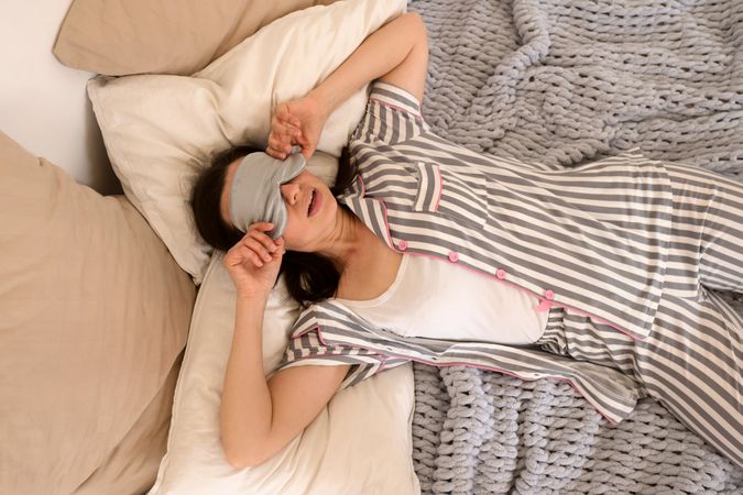 Woman smiling playfully while holding pillows on knit blanket.