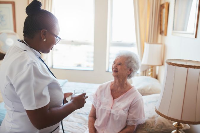 Female nurse giving medicine to older female patient at home