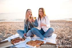 Two women eating pizzas and drinking wine sitting on sand beach 4dMLEb