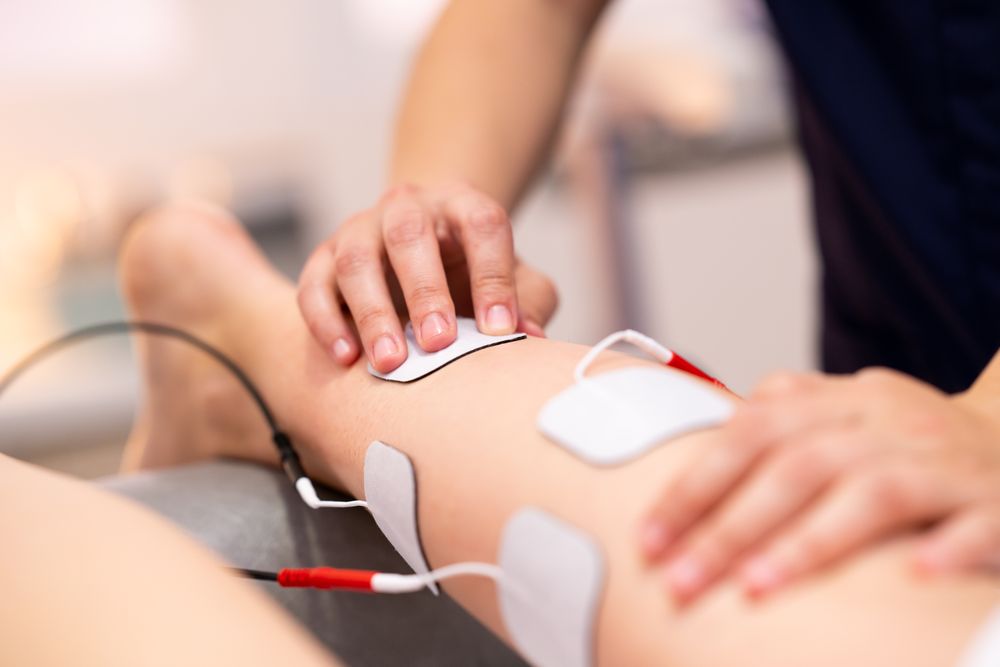 Hands of physio placing electro pads for therapy on calf muscle of patient
