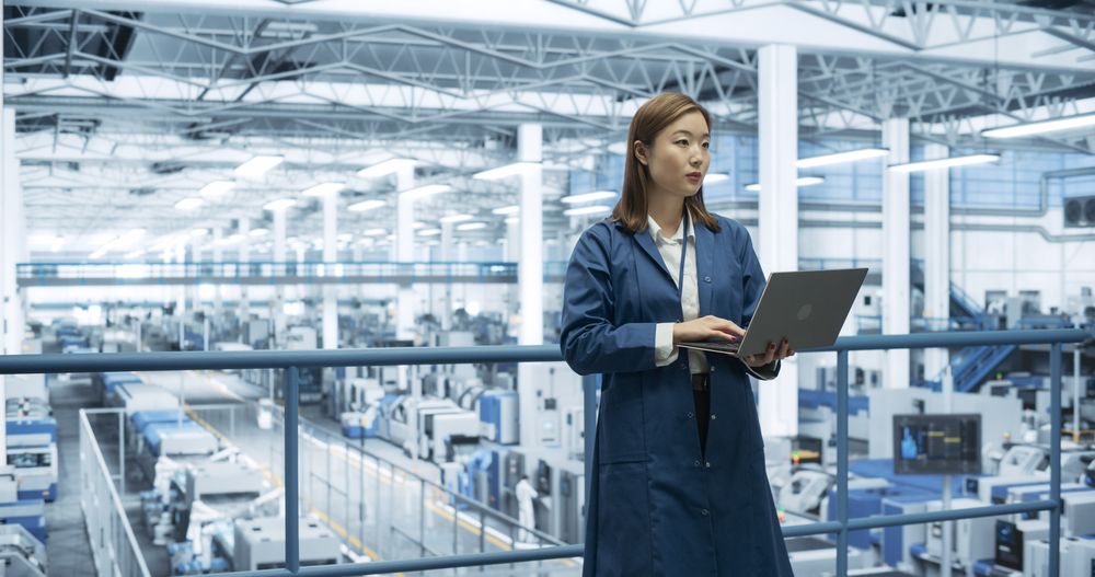 Portrait of a Japanese Engineer Using Laptop Computer and Looking Around a Factory Facility with Equipment Producing Modern Electronic Components for Different Industries