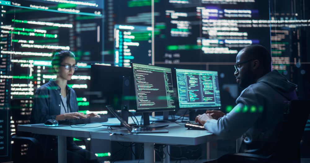 Portrait of Two Diverse Developers Working on Computers, Typing Lines of Code that Appear on Big Screens Surrounding Them.