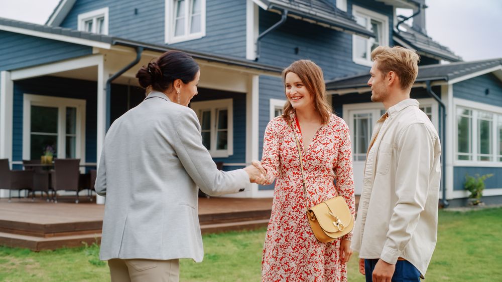 Happy Couple Shaking Hands with Realtor in Front of Their New Home.