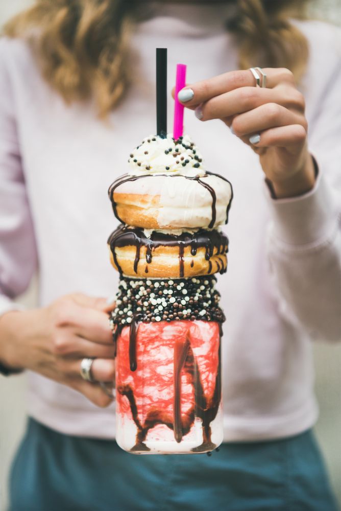 Woman holding stacked donut milkshake with straws, whipped cream, and chocolate sprinkles