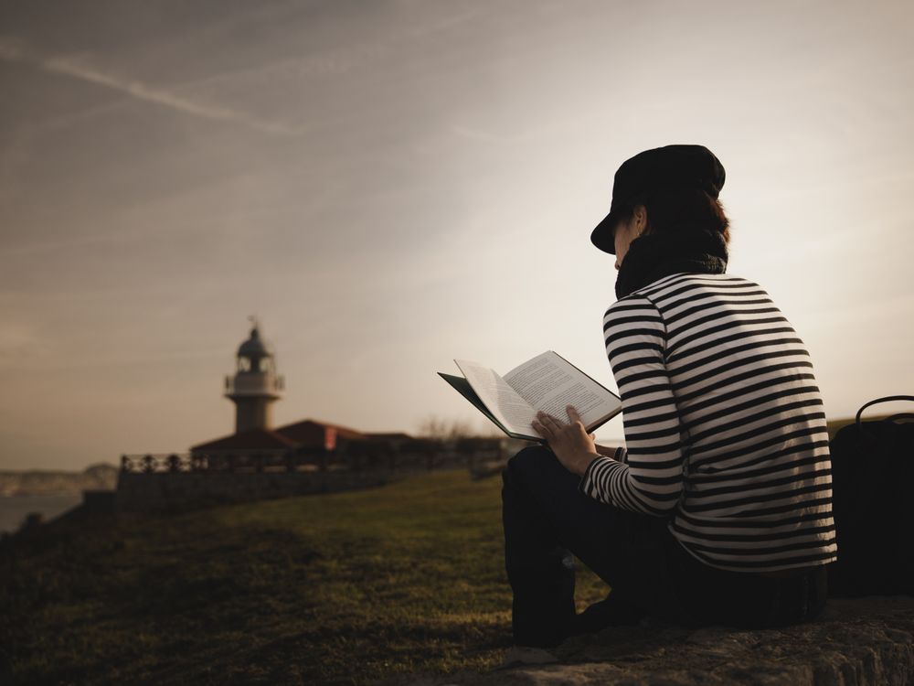 Woman with book on grass near lighthouse