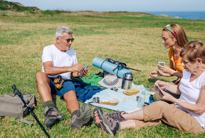 Older parents with adult daughter playing cards during picnic