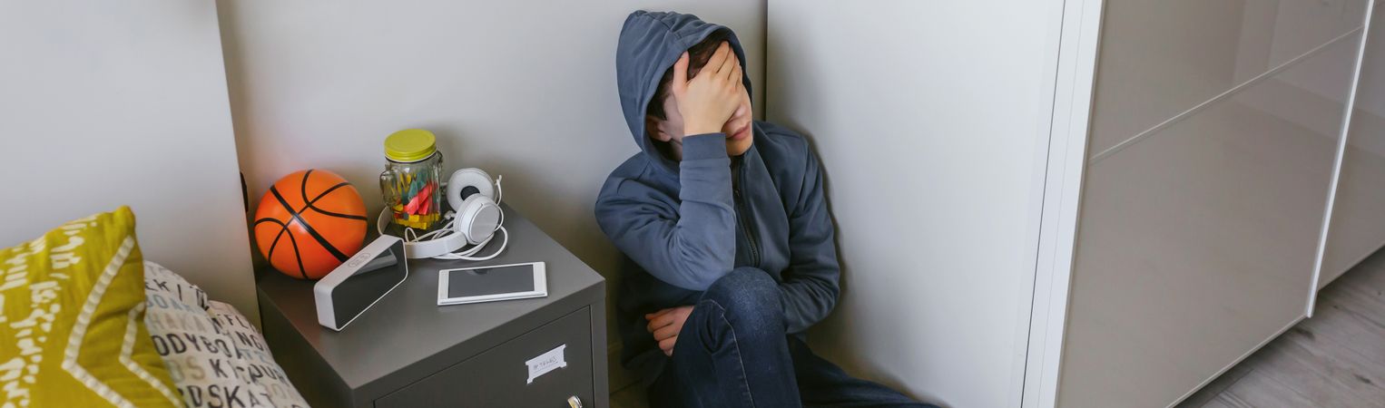 Depressed male teenager sitting on the floor in his bedroom