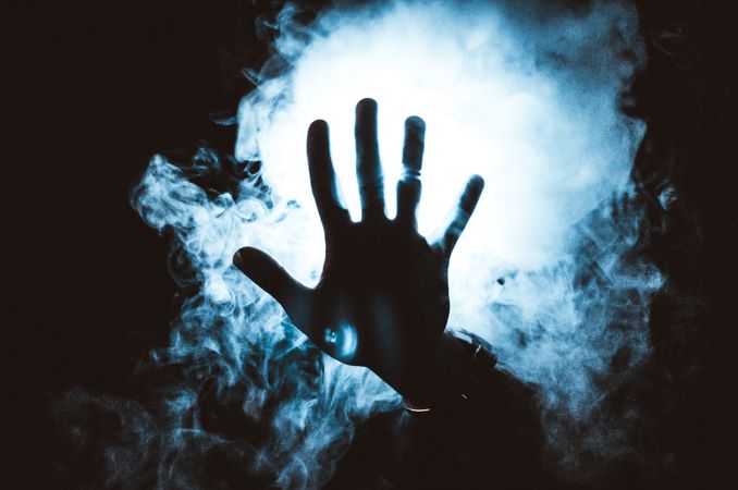Persons 's hand in front of blue light and smoke
