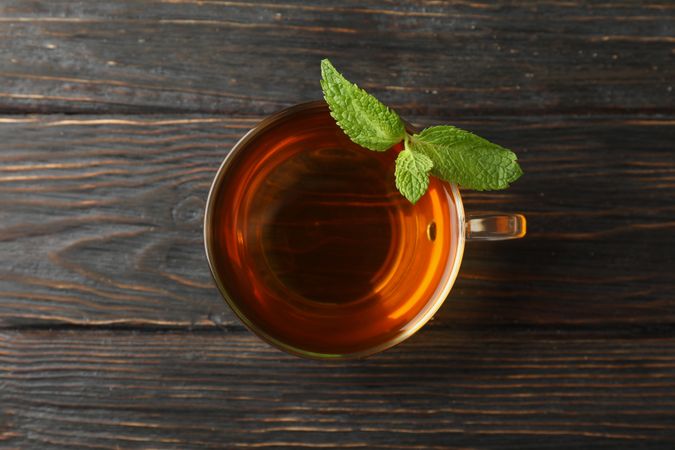 Cup of tea with mint on wooden background, top view