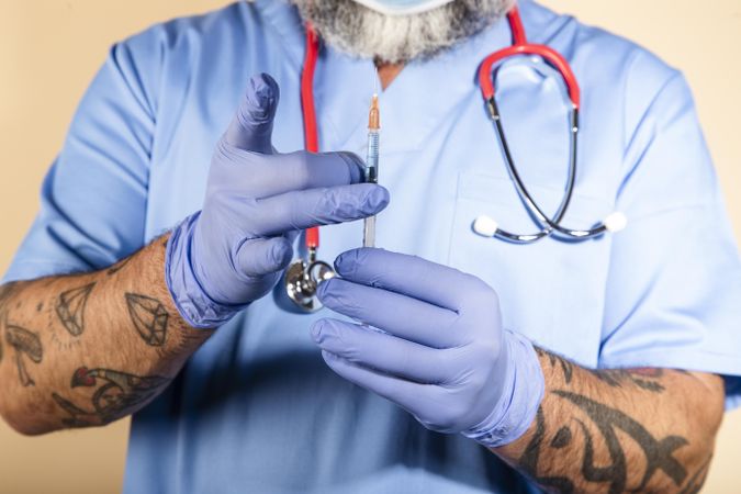 Cropped image of tattooed healthcare worker with stethoscope on neck holding a syringe
