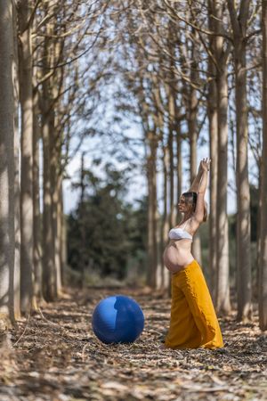 Adult pregnant woman training with pilates ball in park during sunny day