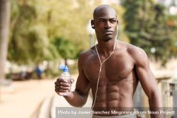 Healthy male with shirt off drinking from a water bottle in an outdoor park 4MR6qb