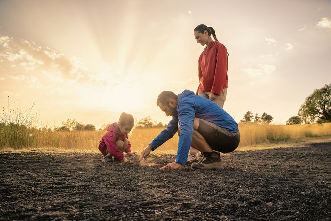 Father and daughter exploring the ground as a family in nature at sunset.