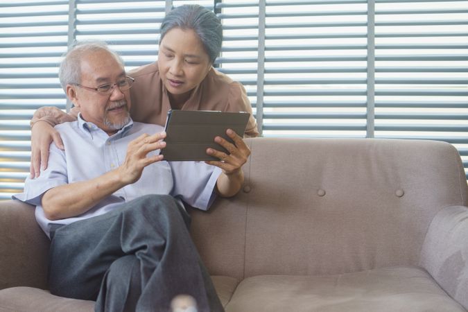 Older Asian couple using digital tablet on sofa