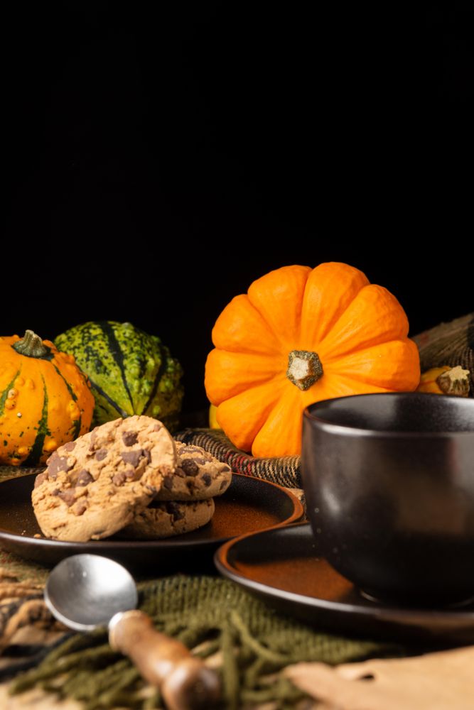 Yellow and green pumpkins beside plate of biscuits on brown wooden table