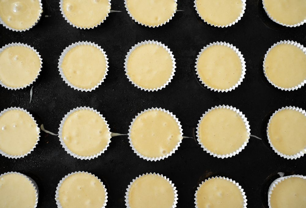 Some paper molds on a baking tray are filled with cupcakes dough