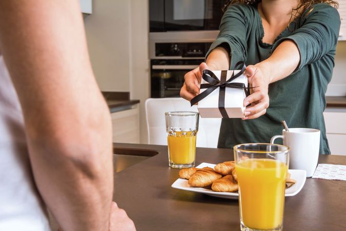 Woman handing man gift over breakfast