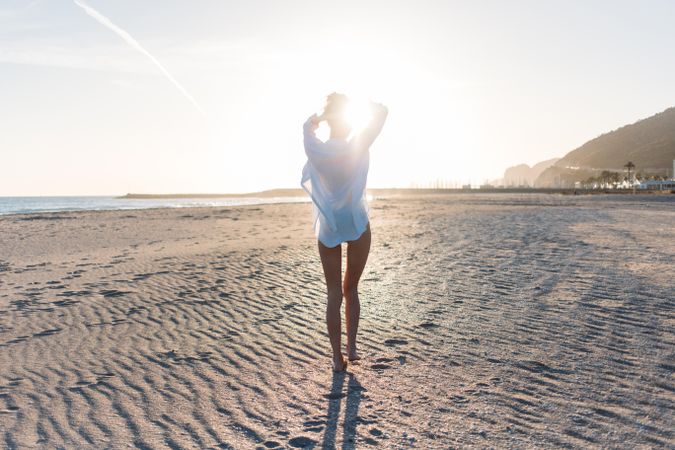 Woman walking towards the sunset on beach in oversized shirt