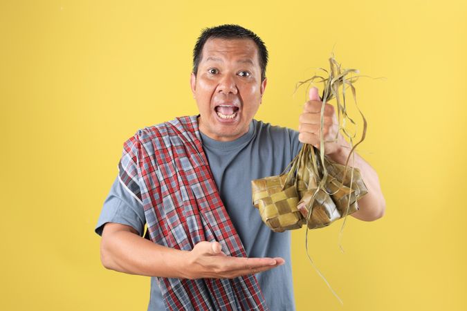 Indonesian Mature Man Wearing Sarung Holding DIamond Shaped Rice Cake or Ketupat