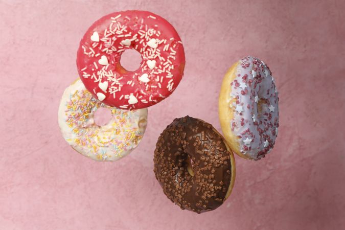 Four different tasty donuts on pink background