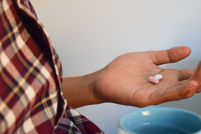 Side view of person with two pills in palm of hand