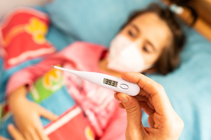 Girl sick in bed with adult taking her temperature