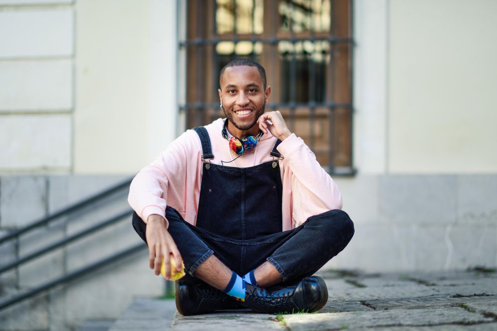 Happy male in overalls and boots sitting cross legged on outdoor steps