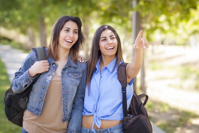 Twin Sisters Wearing Backpacks and Pointing Outside