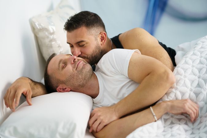 Two males kissing each other in bed