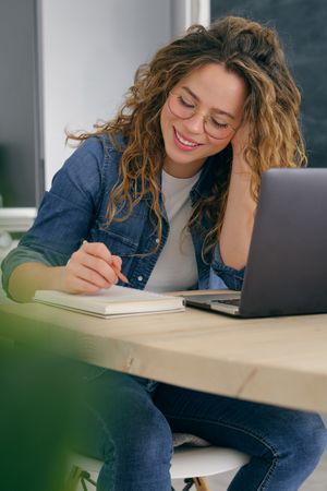 Smiling woman taking notes in notebook at table