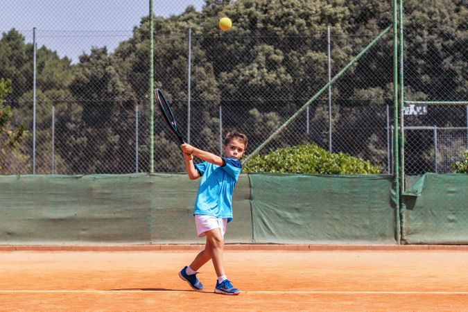 Little boy playing tennis on a dirt court