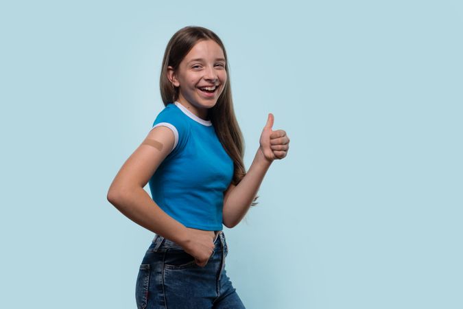 Young girl smiling and giving thumbs-up after vaccination.