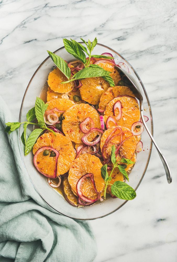 Mediterranean orange dish with onions, mint, and silver serving spoon on marble background