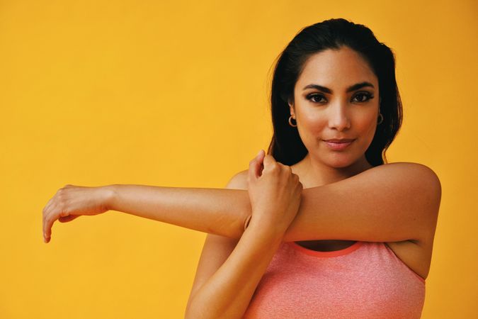 Hispanic woman in yoga clothes stretching her arm in yellow studio, copy space