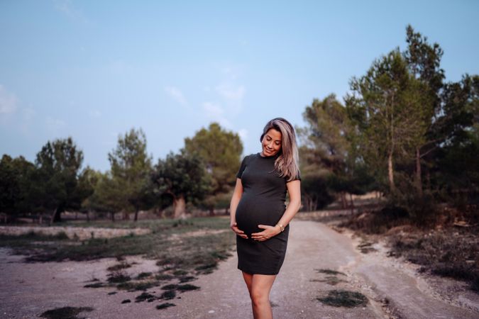 Charming pregnant woman standing on walkway in park