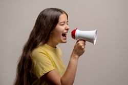 A young woman shouting loudly into a megaphone to make an announcement or protest.