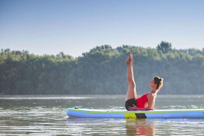 Woman with her legs up in stretch on paddleboard in the morning