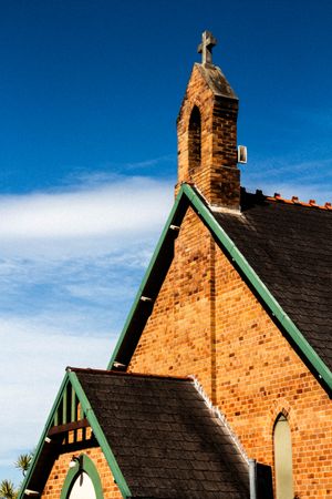 Close-Up Of The Rooftop And Cross Of A Historic Brick Church Against A Blue Sky