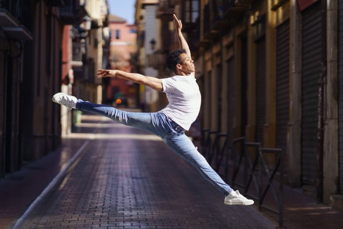 Flexible male dancer in jeans and t-shirt leaping on an empty European street