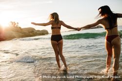 Women in bikini holding hands and running on sea water 0WeEO4