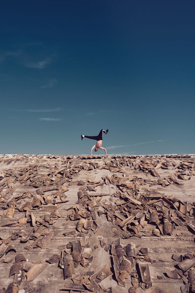 Anonymous man dancing breakdance on rooftop in sunny day