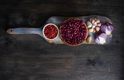 Wooden cutting board with bowl of kidneys, red peppercorns, bulb of garlic and onion half
