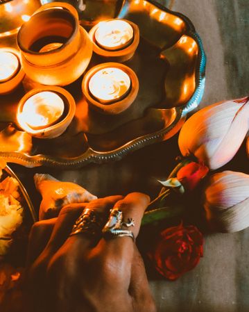 Cropped image of a hand holding a flower beside tray of lit diyas