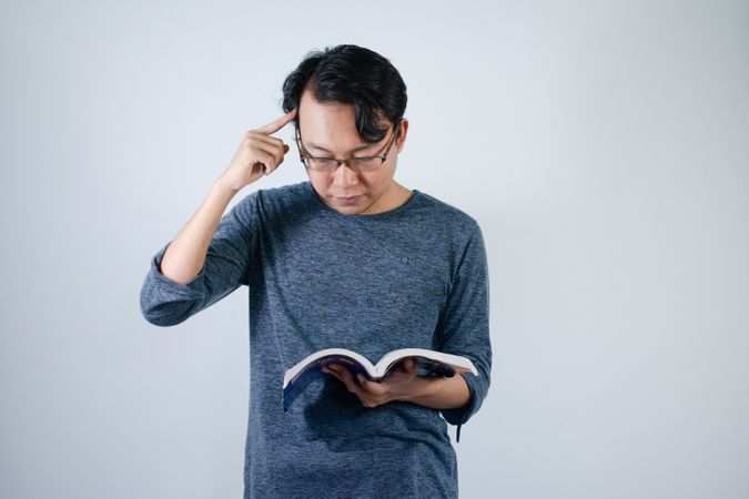Asian young male reading book with thinking gesture