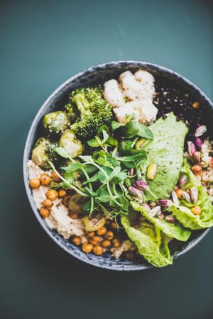 Healthy vegetarian bowl pictured on green surface, vertical composition