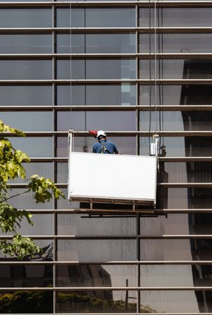 Faceless male window washer cleaning high building facade in construction