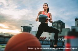 Female athlete doing forward lunges holding a medicine ball on rooftop 42QjK5