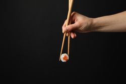 Female hand with chopsticks hold sushi roll on dark background. Japanese food